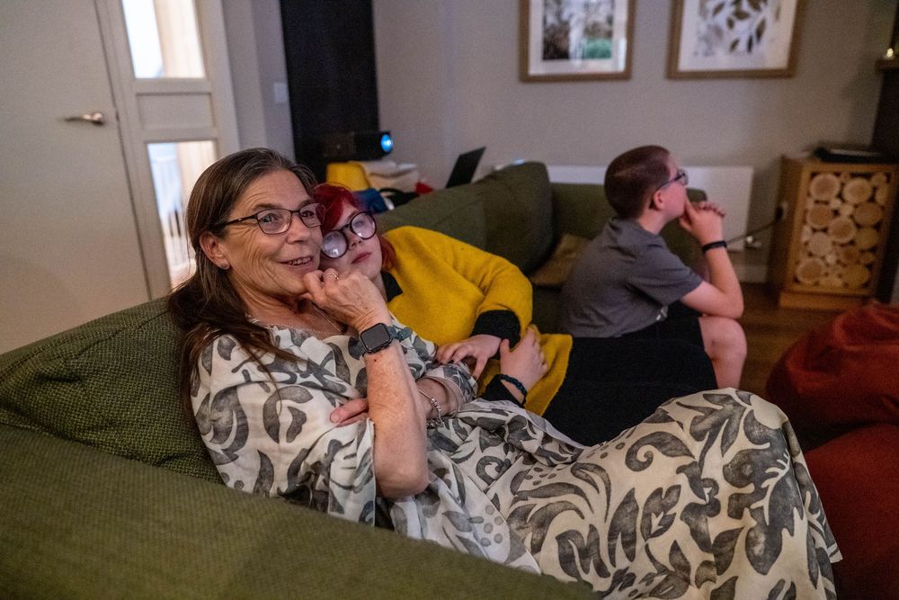 People relax on a green couch while watching TV in a cozy living room with wall art and decorations.
