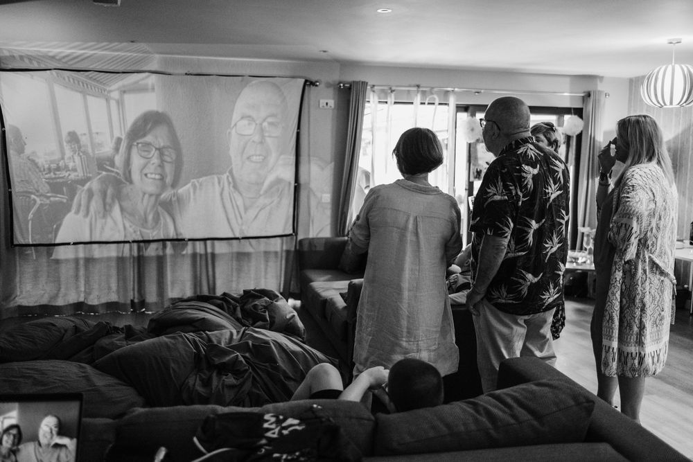 People watching a video presentation in a dimly lit room with some audience members lying on floor mats.