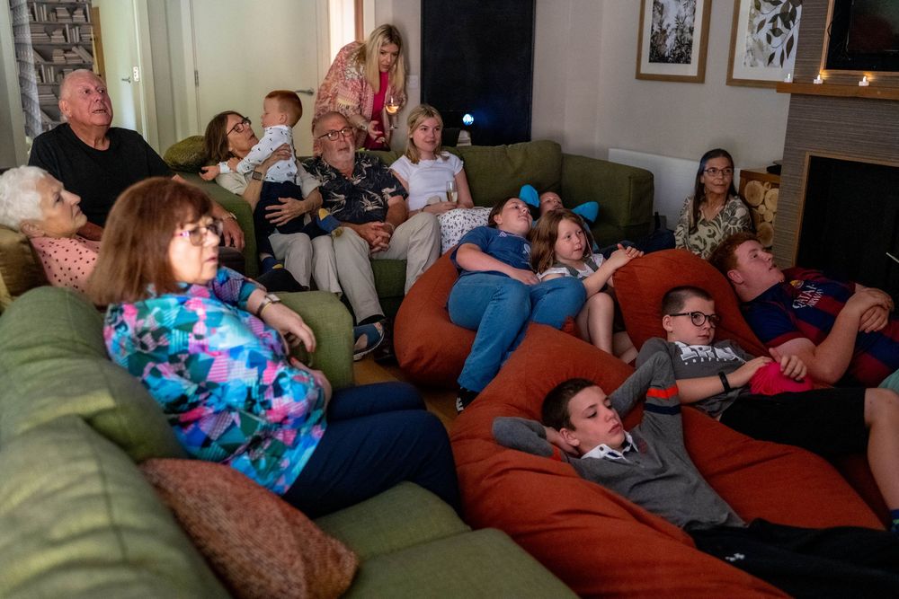 A group of people lounging on couches while watching TV or a movie together in a living room.
