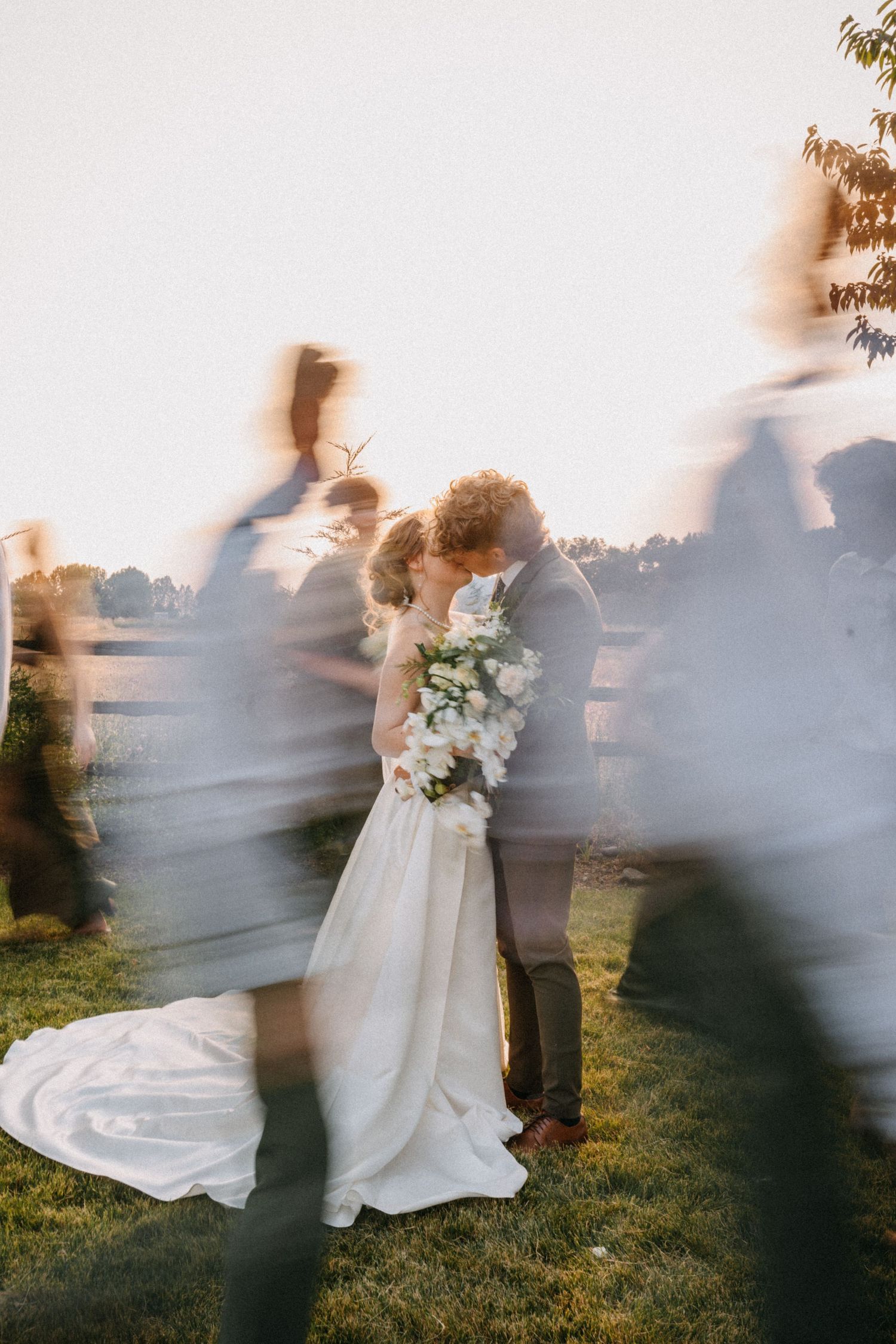 Artistic motion blur wedding photo with ghosted figures surrounding newlyweds in golden light.