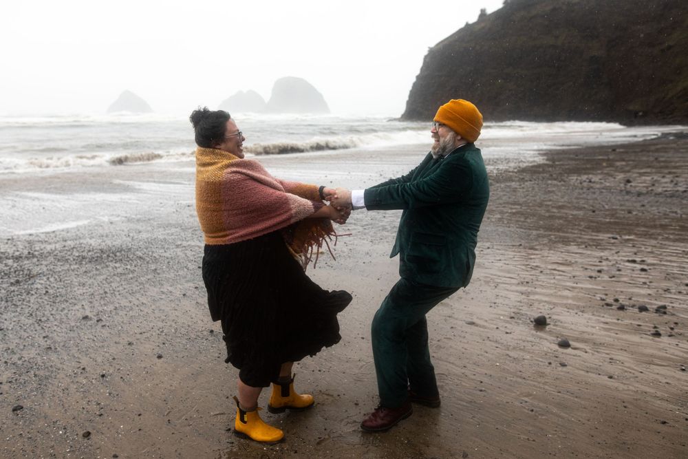 Two people dance playfully on a misty beach with dramatic coastal cliffs in the background.