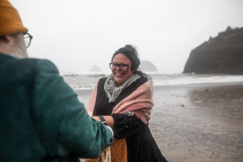 People share a joyful moment together on a misty beach with cliffs in the background.