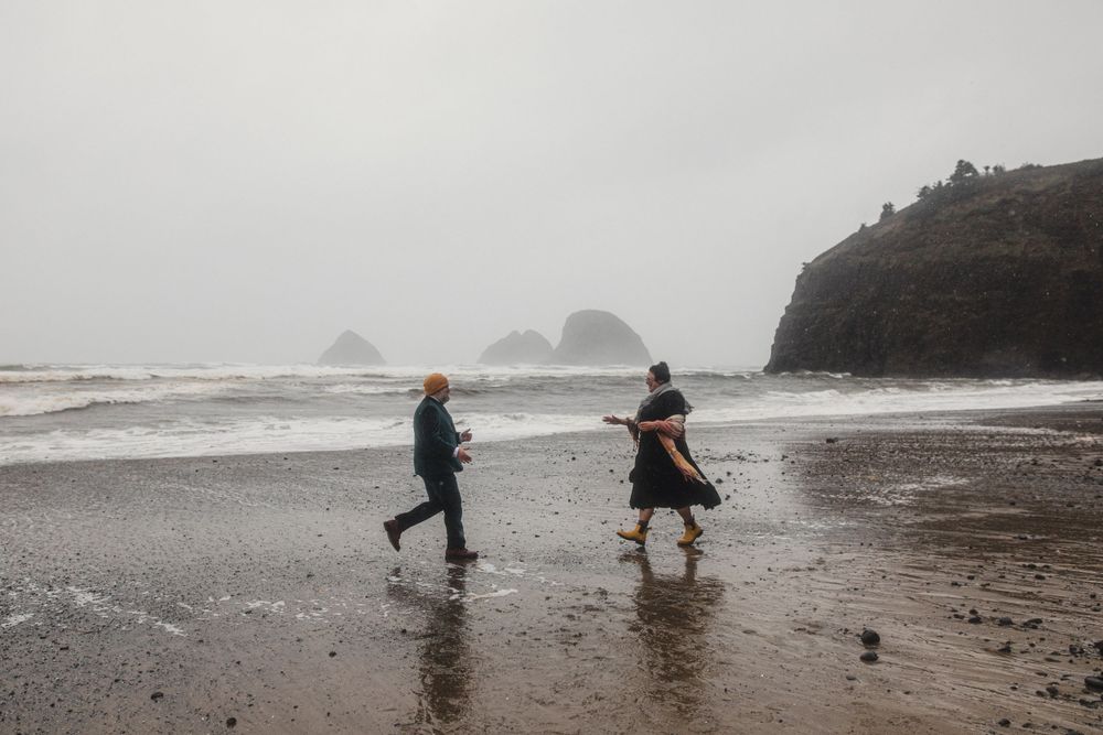 Friends dance and play on a moody beach with distant sea stacks visible through the mist.