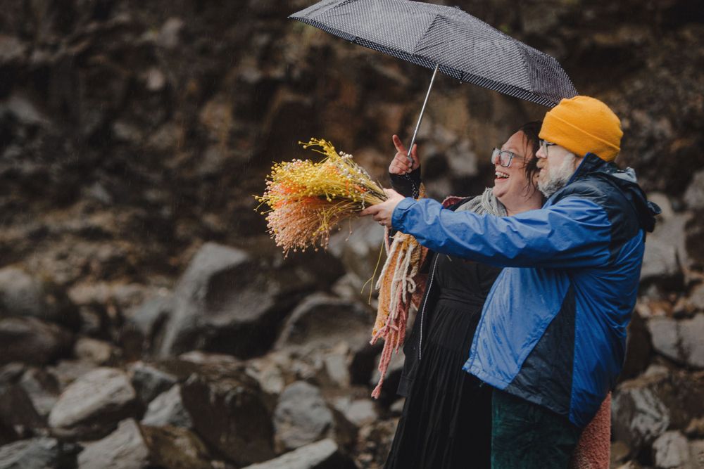 Two people embrace under an umbrella on rocky coastal cliffs during overcast weather.