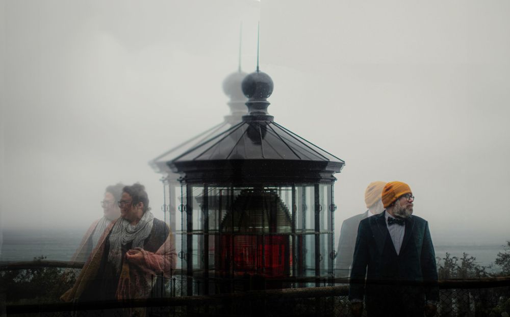 Silhouettes stand near a historic lighthouse tower on a misty coastal overlook.