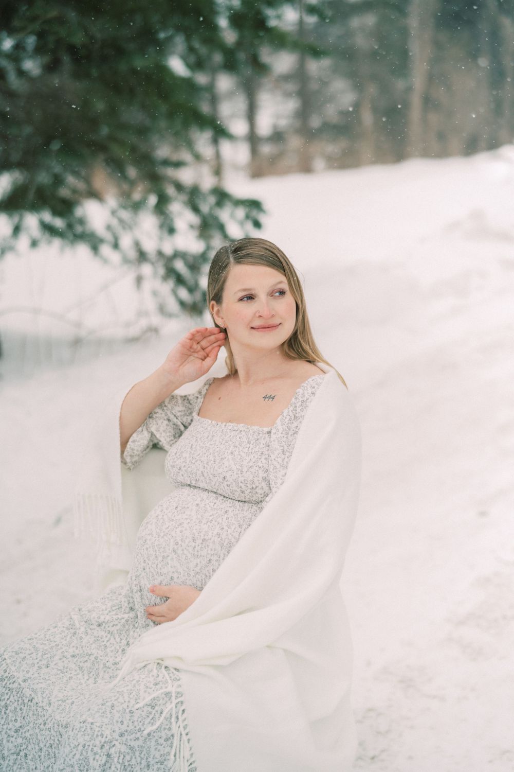 Winter maternity photo shoot in a snowy forest setting with delicate white and silver styling.