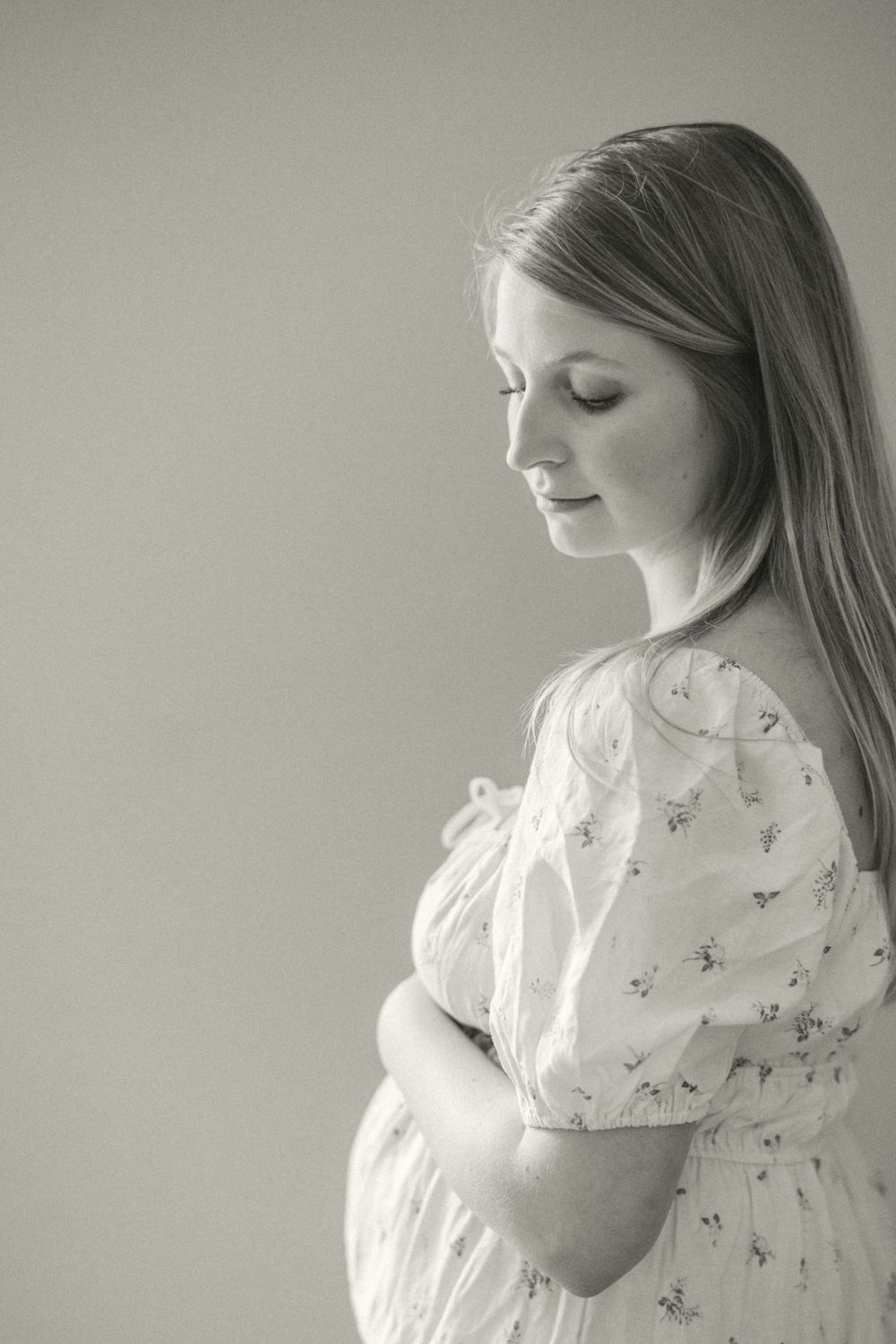 Black and white profile portrait of a pregnant woman in a floral dress holding her belly against a light background.