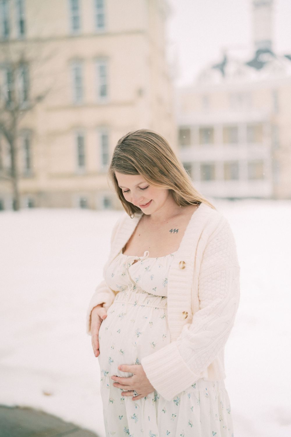 Maternal scene in winter with figure wearing white floral dress and cardigan against snowy backdrop.