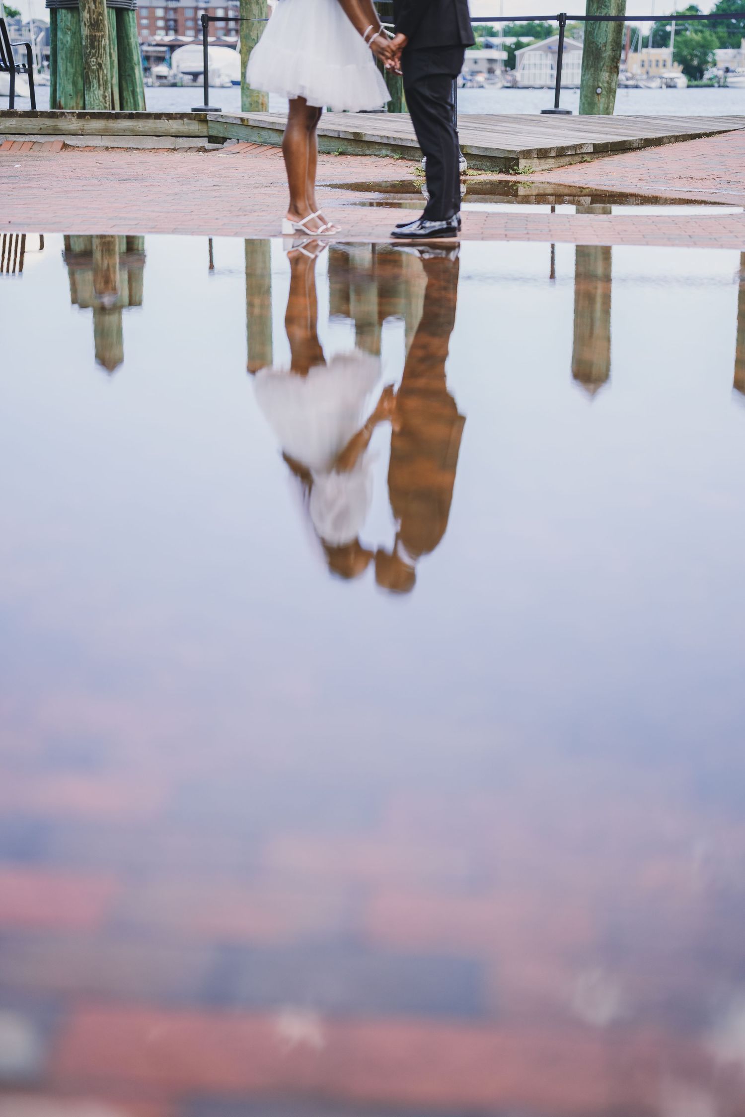 A romantic couple embraces by a reflective pond in a lush green forest setting during golden hour.