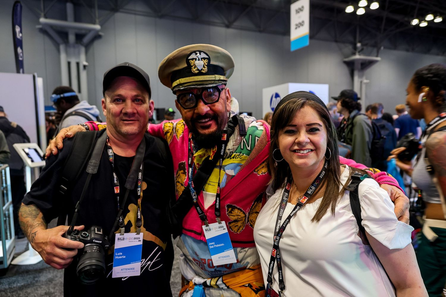 Three attendees pose together at a convention wearing colorful attire and conference badges.