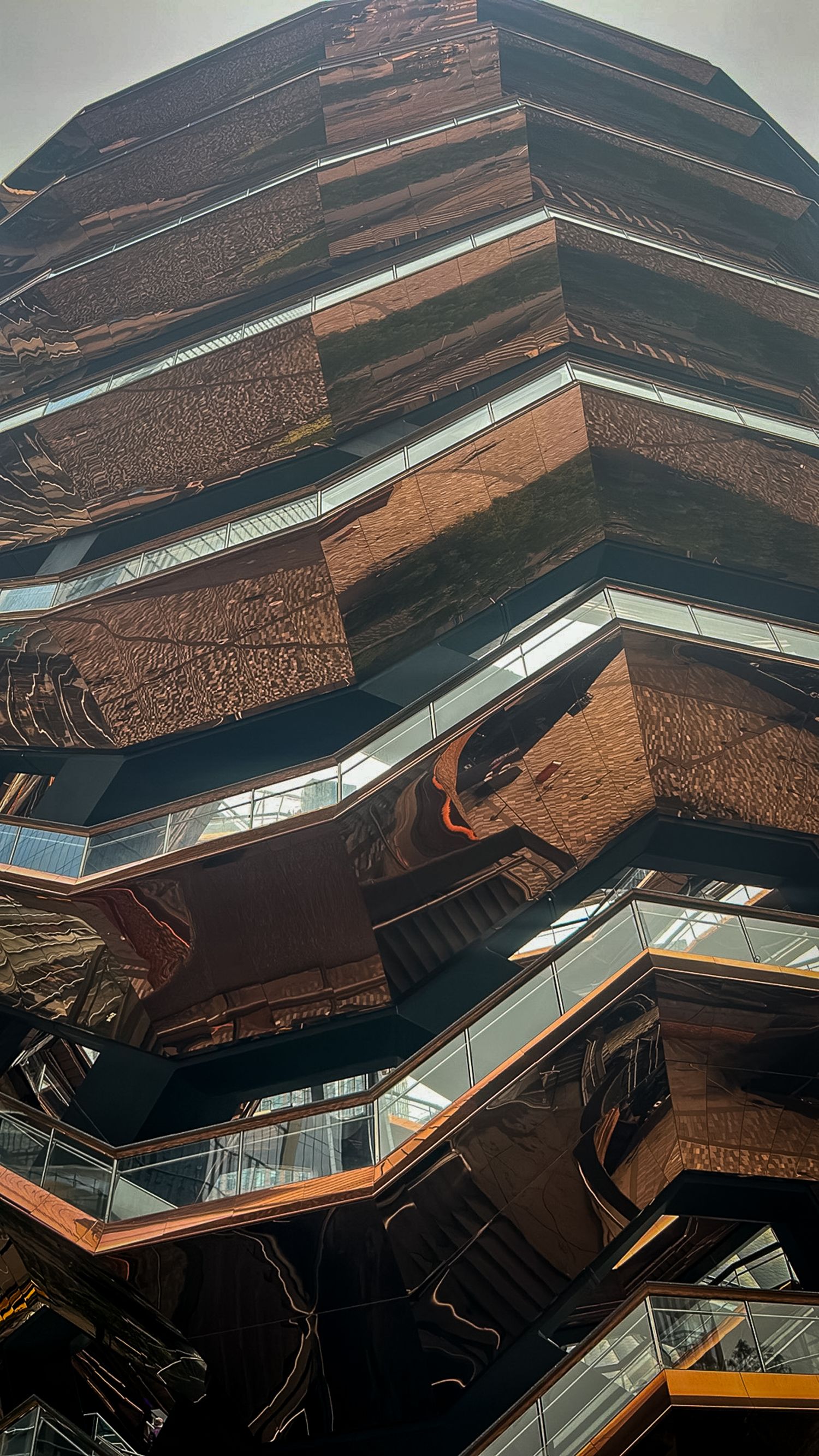 Modern architectural building with zigzag balconies and copper-toned reflective surfaces captured from a dramatic low angle.