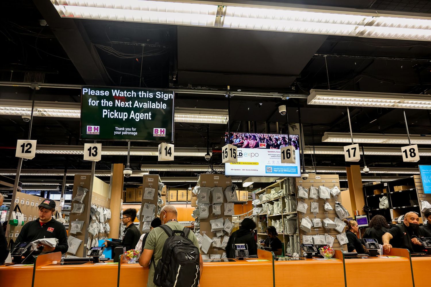 Grocery store checkout lines with shoppers and digital displays in a well-lit retail environment.