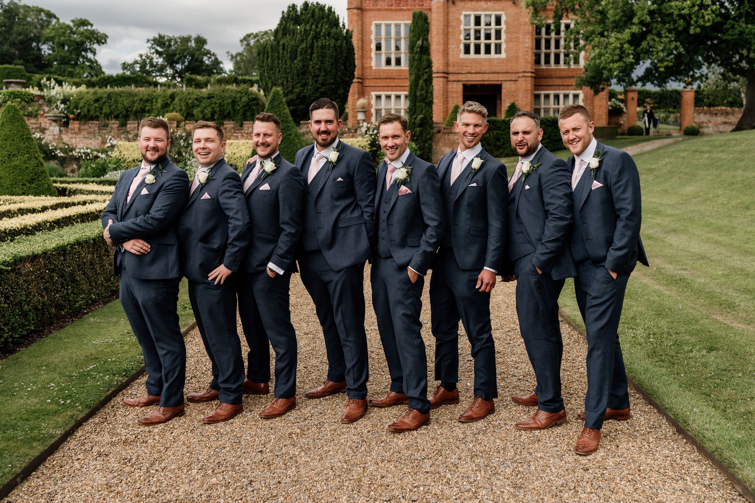 Groomsmen in matching navy suits posing together on estate grounds.