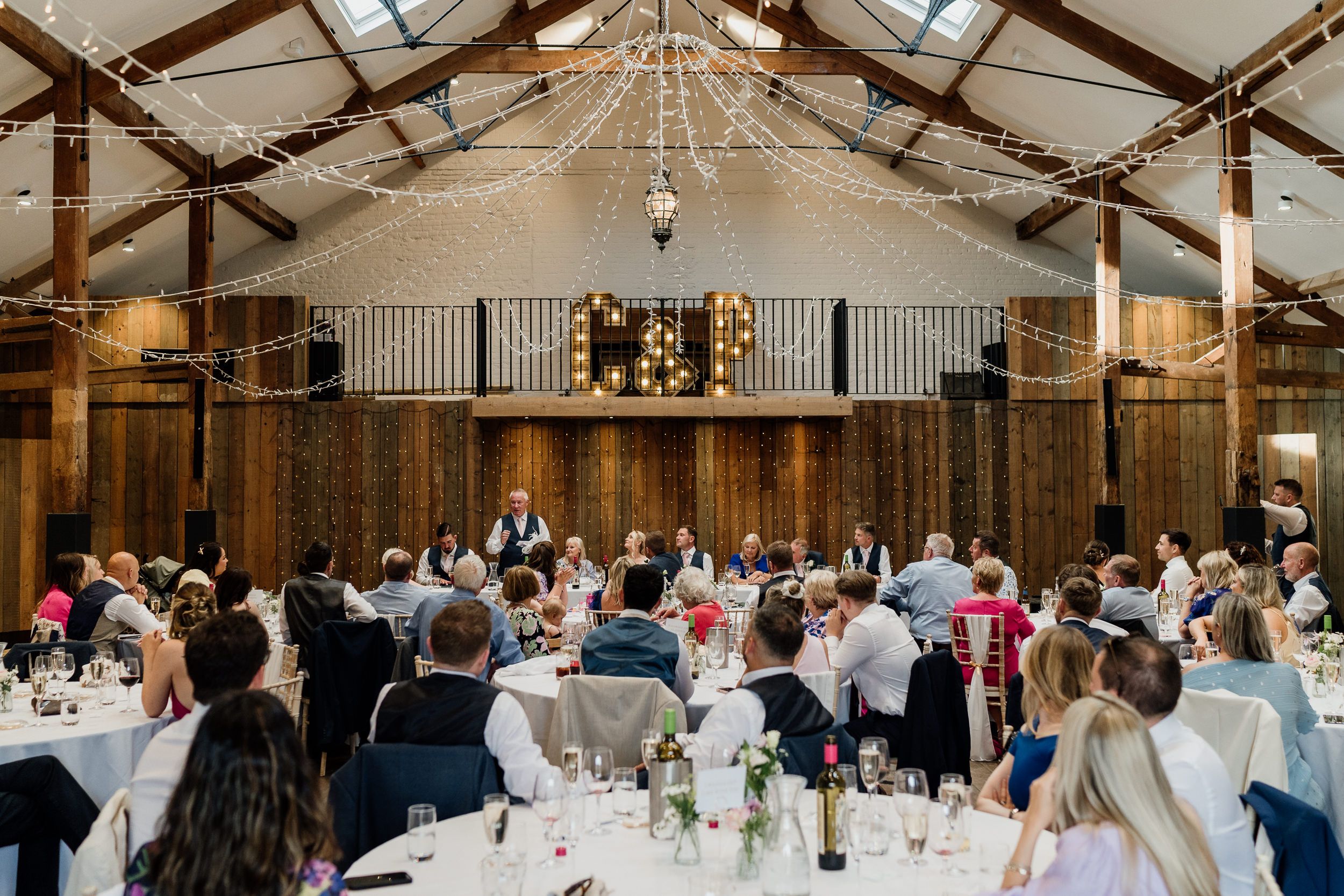Panoramic view of an elegant rustic barn wedding reception at Oxnead Hall with exposed wooden beams and white table settings.