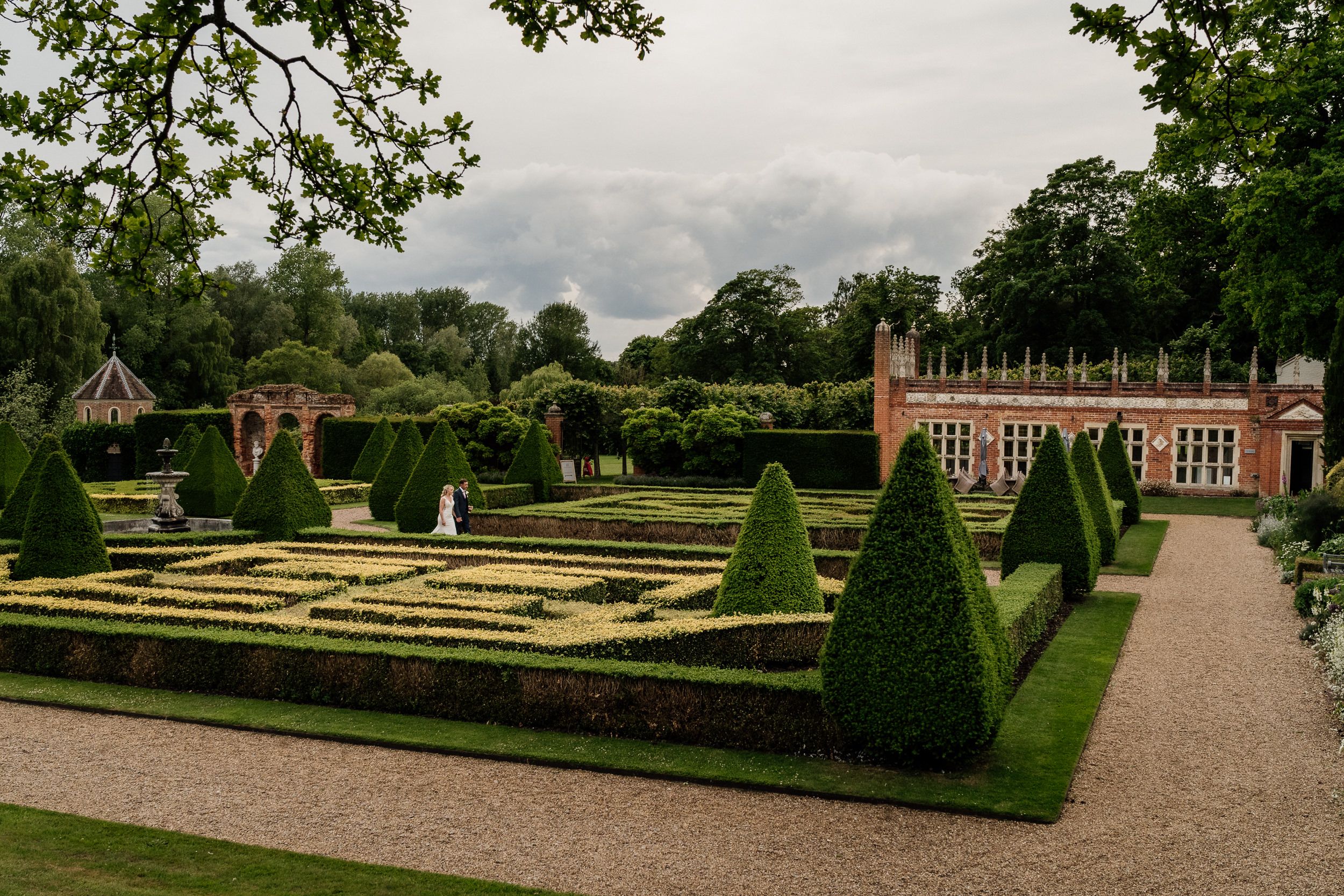 A panoramic view of a formal English garden at Oxnead Hall manicured hedges, topiary bushes, and a historic brick mansion in the distance.