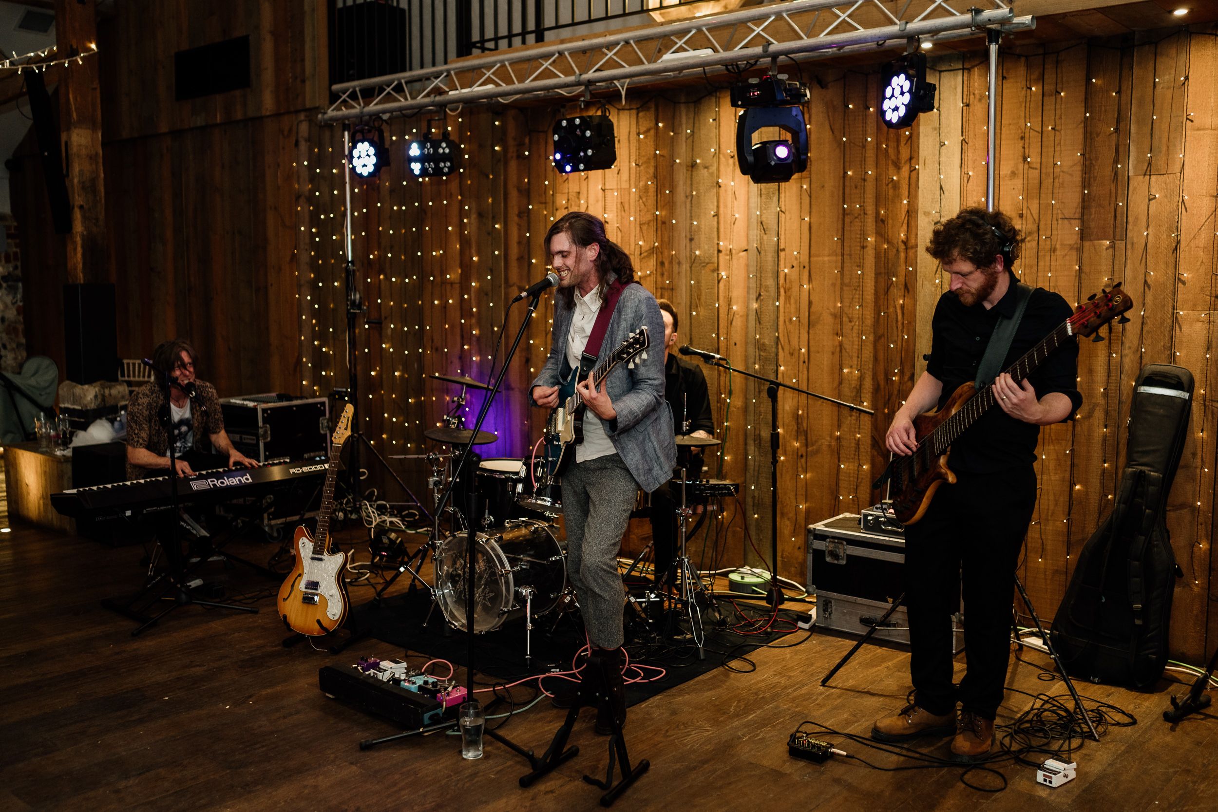 Musicians perform in a rustic wood-paneled venue with stage lighting and sound equipment setup.
