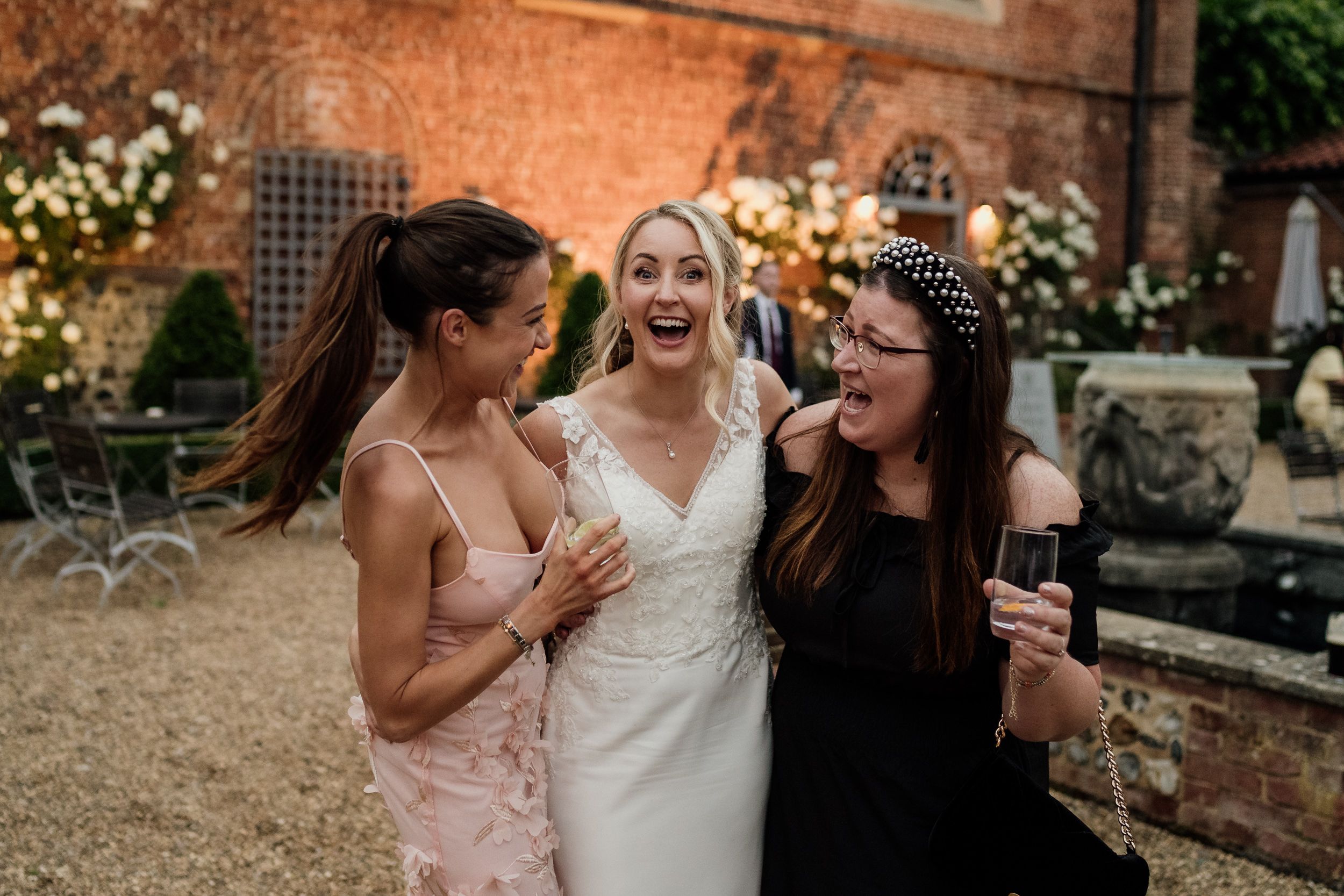 Three bridesmaids in light pink dresses laugh and share a joyful moment together during wedding celebrations.