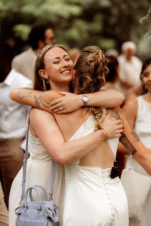 A group of figures wearing white outfits share an emotional embrace during a summer celebration.