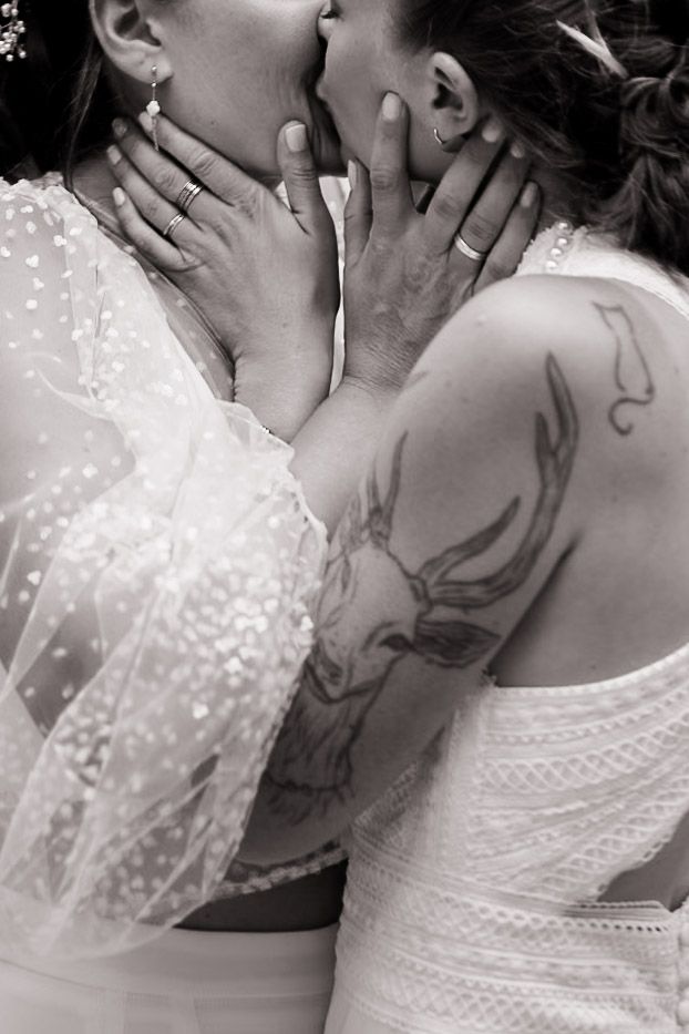 Close up of a couple in wedding attire sharing an intimate kiss with sheer lace dress detail visible in monochrome.