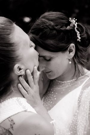 Black and white intimate wedding photograph showing two people in white dresses sharing a tender moment while embracing.
