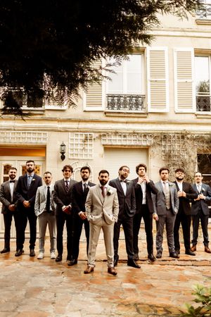 A line of groomsmen in suits stand together outside a building in vintage sepia tones.
