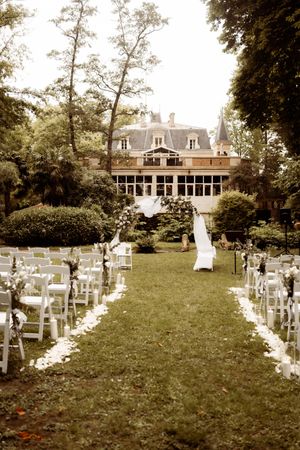 Vintage sepia-toned outdoor wedding venue setup with white chairs lining a grass aisle leading to a grand mansion.