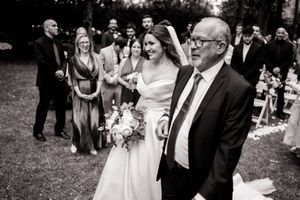 A black and white wedding photo shows a happy bride in a white dress walking with an elderly gentleman at an outdoor ceremony.