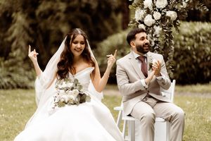 A couple shares a lighthearted moment during their outdoor wedding ceremony with a beige suit and white dress.