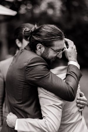 Black and white photo capturing an emotional embrace between two people at what appears to be a wedding ceremony.