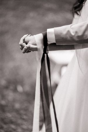 A black and white detail shot of hands holding a dress strap or belt against a blurred background.
