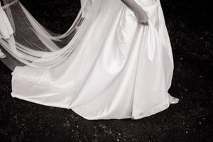 A flowing white dress hem sweeps across dark ground in black and white artistic composition.