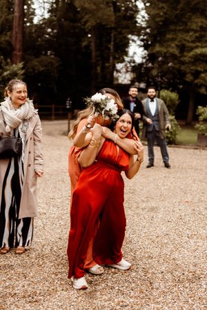 People in wedding attire share emotional reactions while playing a game scattering fall leaves in an outdoor setting.