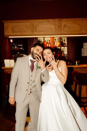 A wedding couple shares a playful and joyful moment together at a dimly lit reception venue.