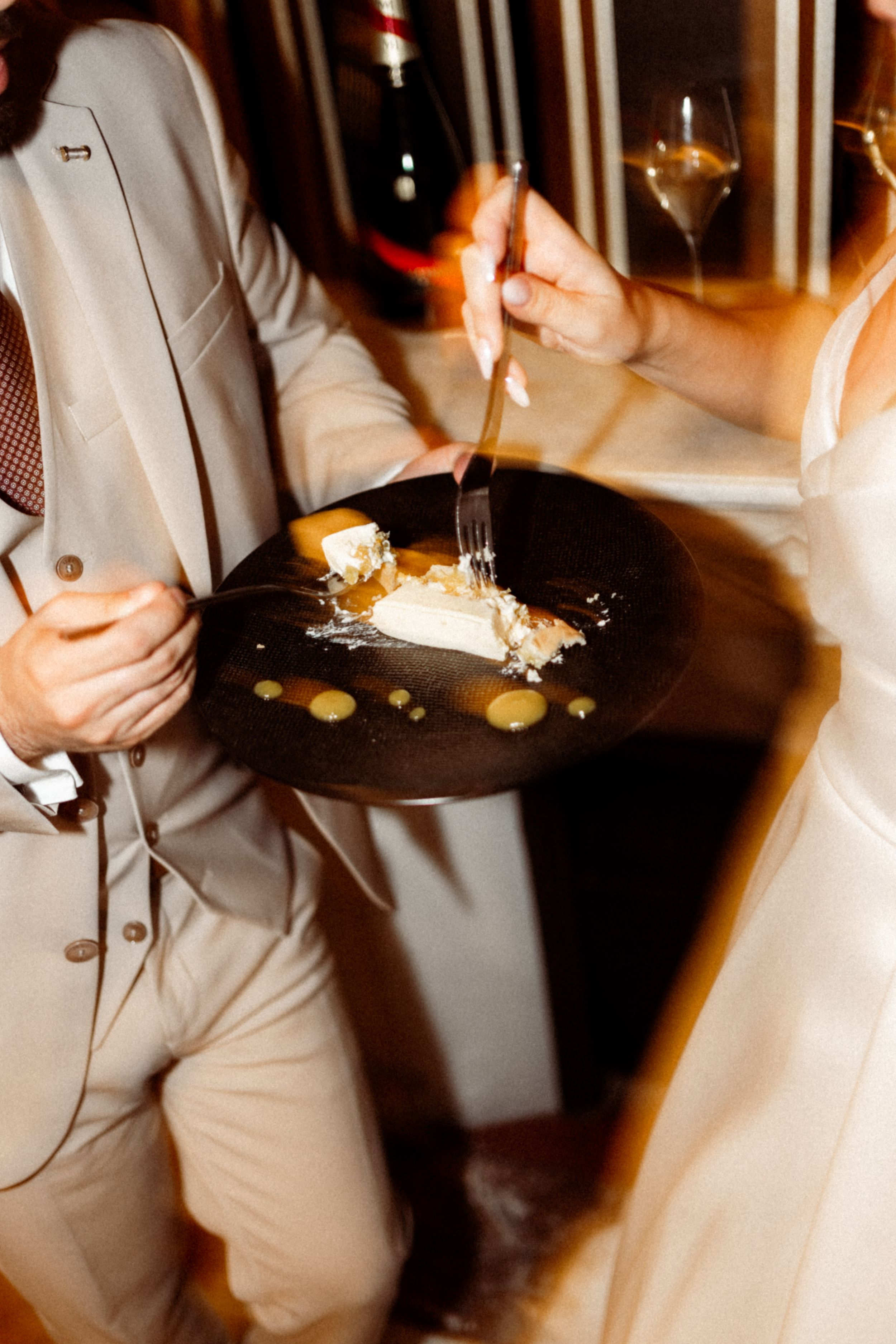 Two people in formal attire share an elegant dessert at an upscale restaurant with atmospheric lighting.