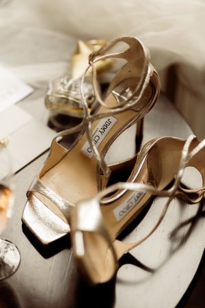 A pair of elegant Jimmy Choo gold metallic strappy high heel sandals displayed on a light fabric surface.