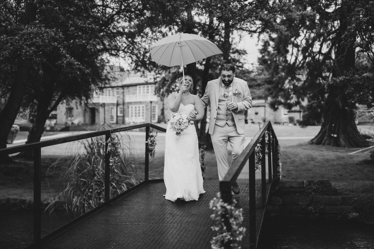 Bride and groom walking across the bridge in the rain. Both are laughing.