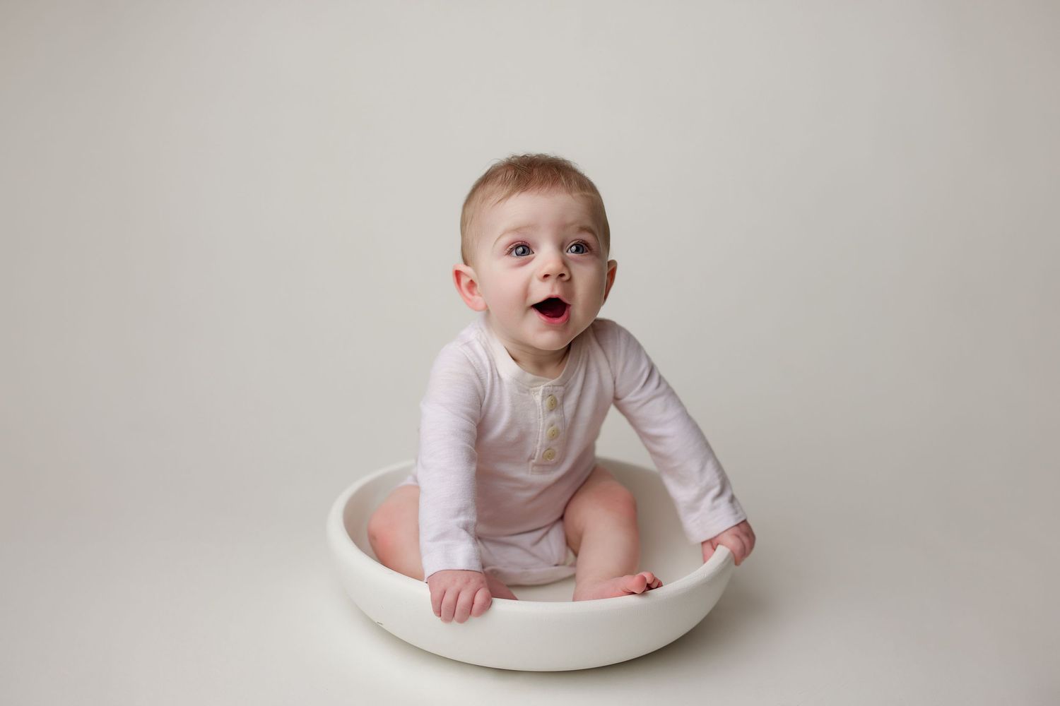 Six month old baby poses progressively getting up from lying down in white studio setup.