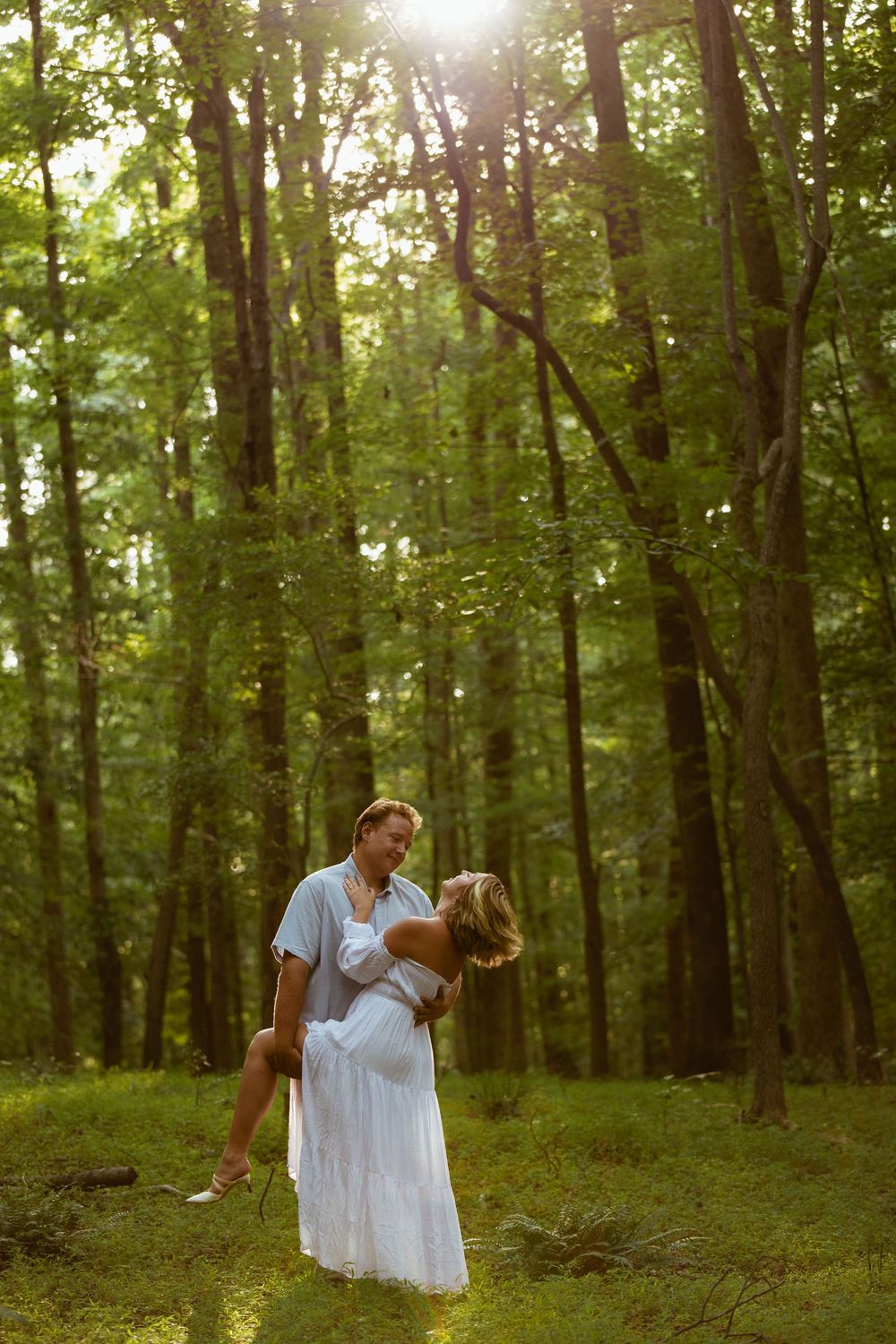 Dancing couple spins through sunlit forest clearing in romantic moment.