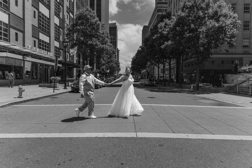 Black and white photo of couple dancing in urban street with tall buildings in background.