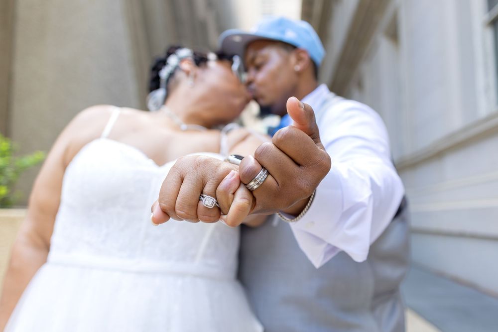 Close-up of newlyweds holding hands and showing wedding rings in outdoor setting.