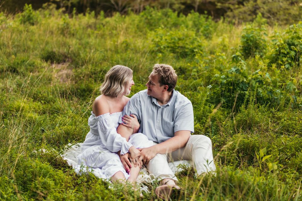 Couple lounges together in sunny meadow with vibrant green grass.