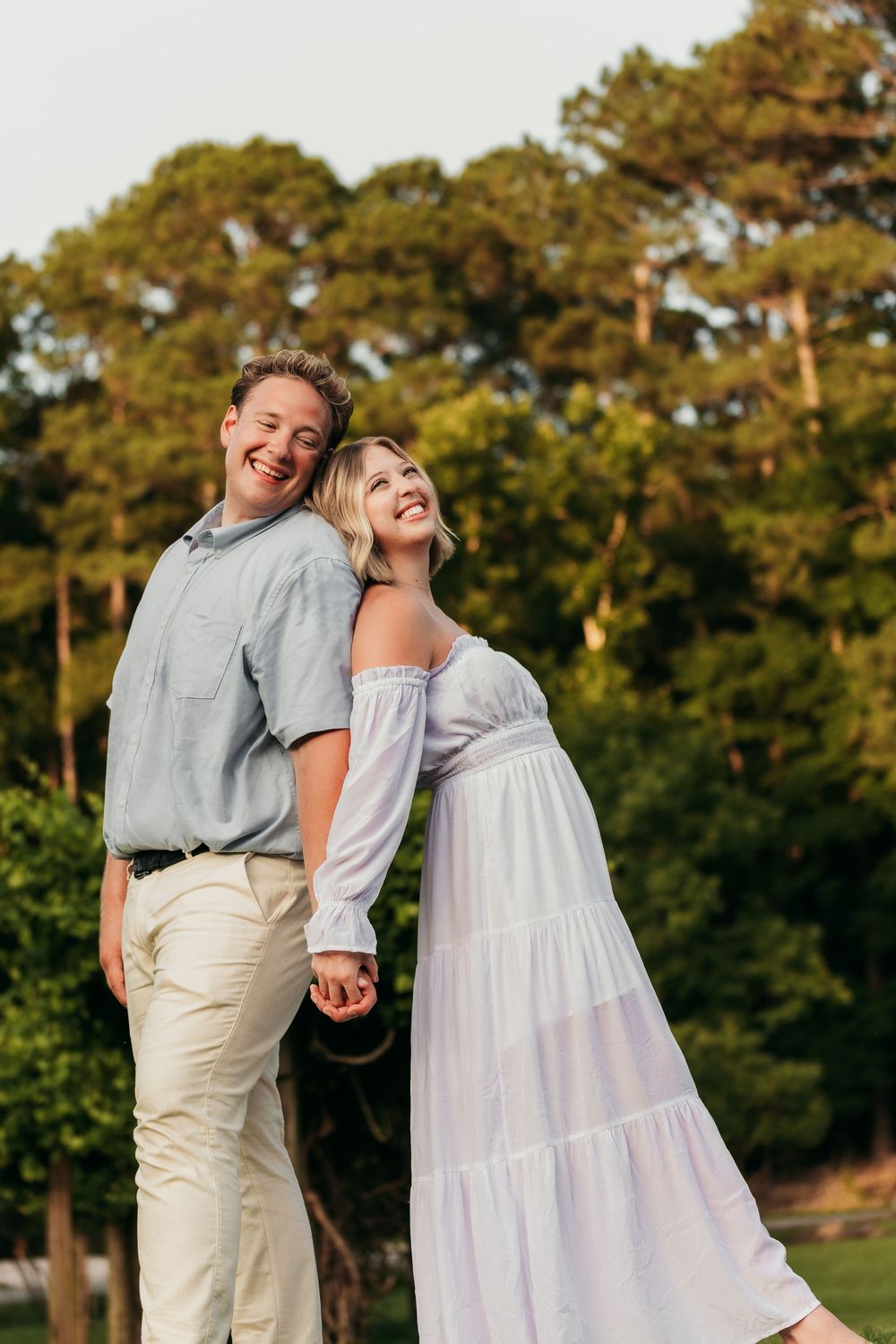 Couple laughs together outdoors against backdrop of golden pine trees.