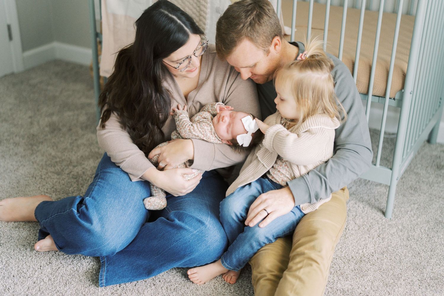 Family sitting on carpeted floor together in intimate moment with soft natural lighting.