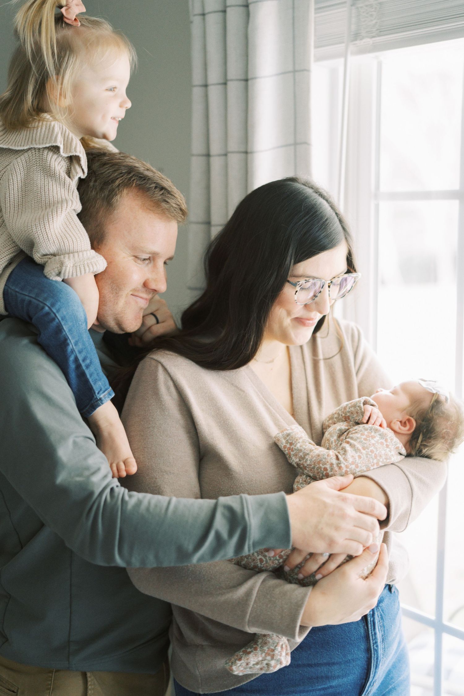 Loving family moment by window with baby and toddler in cozy home setting.