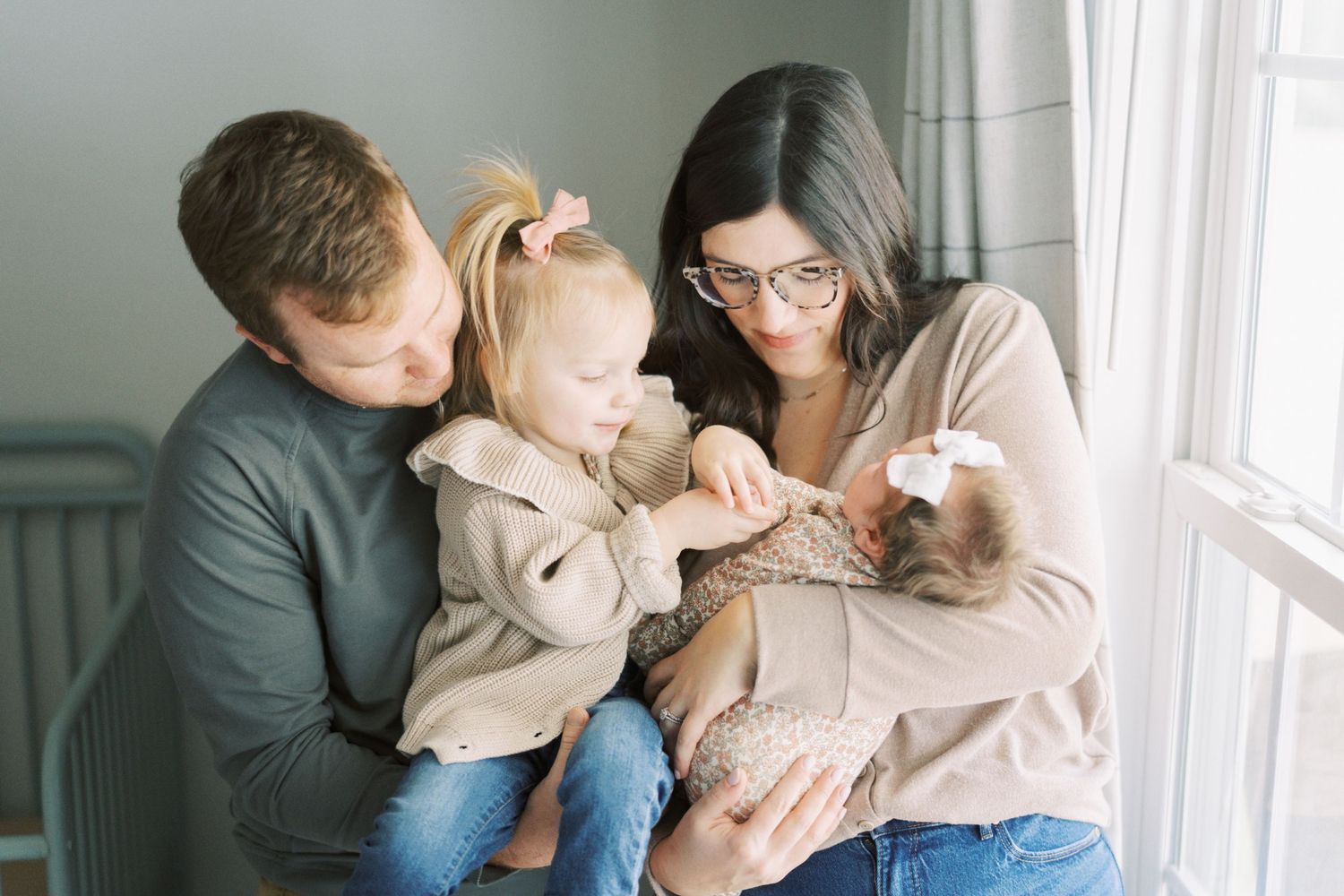 Family gathers by window in cozy living room sharing tender moment together in natural lighting.