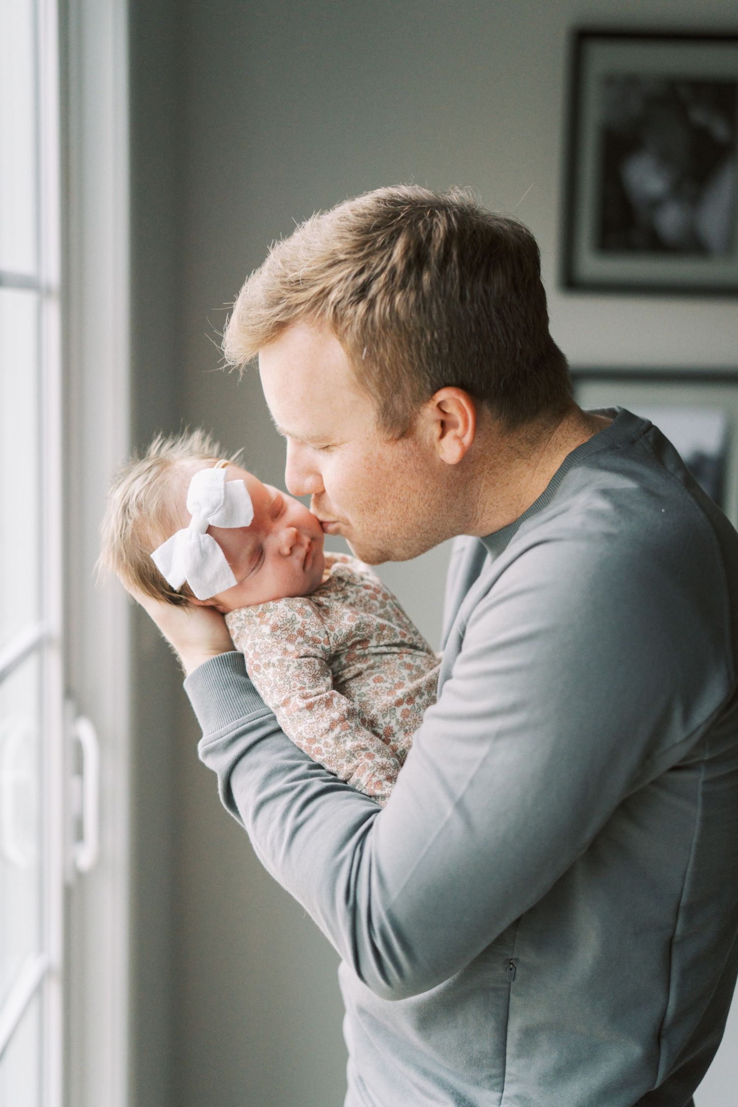 A tender moment between parent and infant by a bright window.