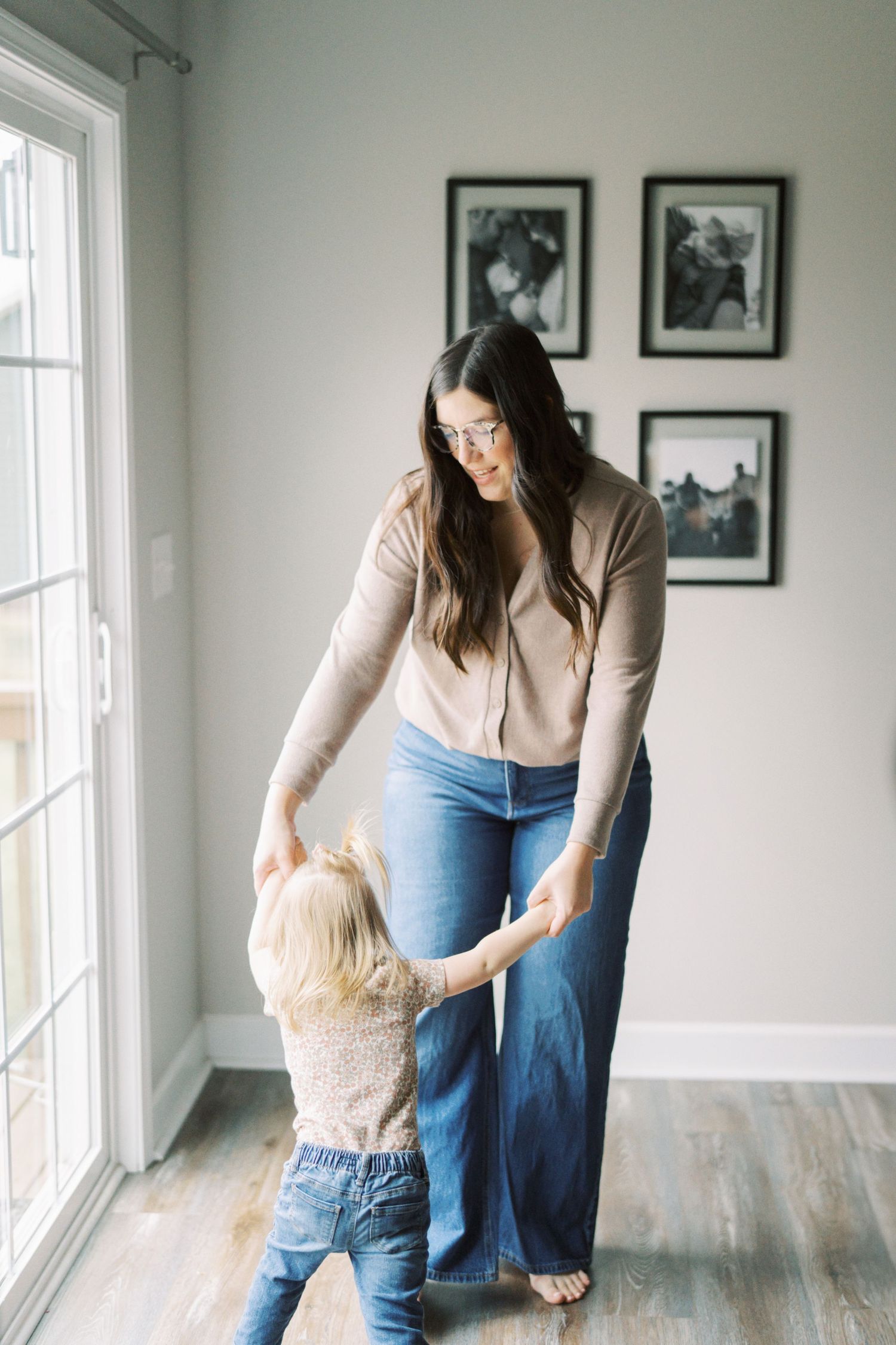 A parent and toddler share a sweet moment while dancing by a sunlit window.