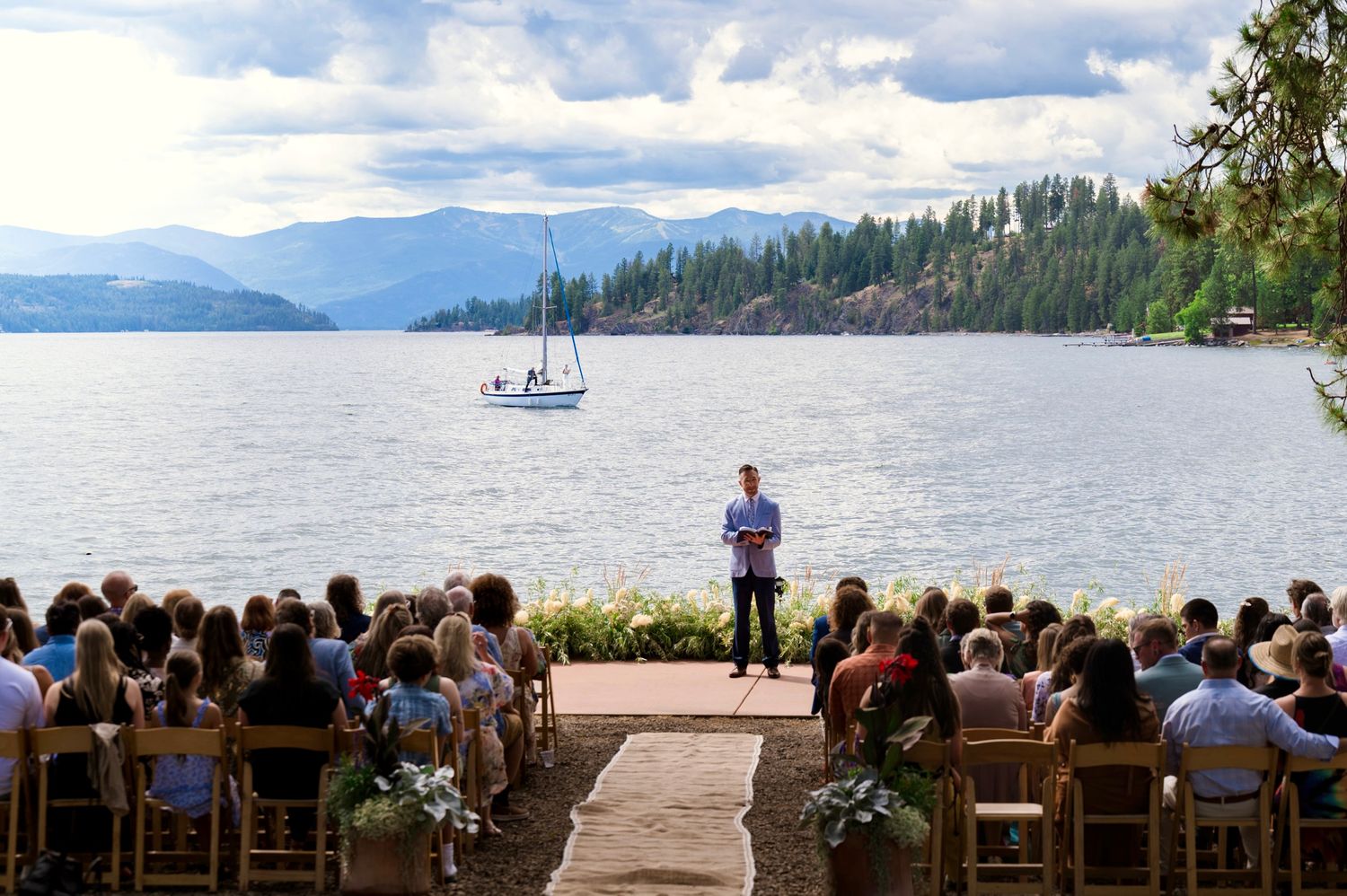Scenic view of a lake surrounded by mountains and forest with a boat visible in the distance.