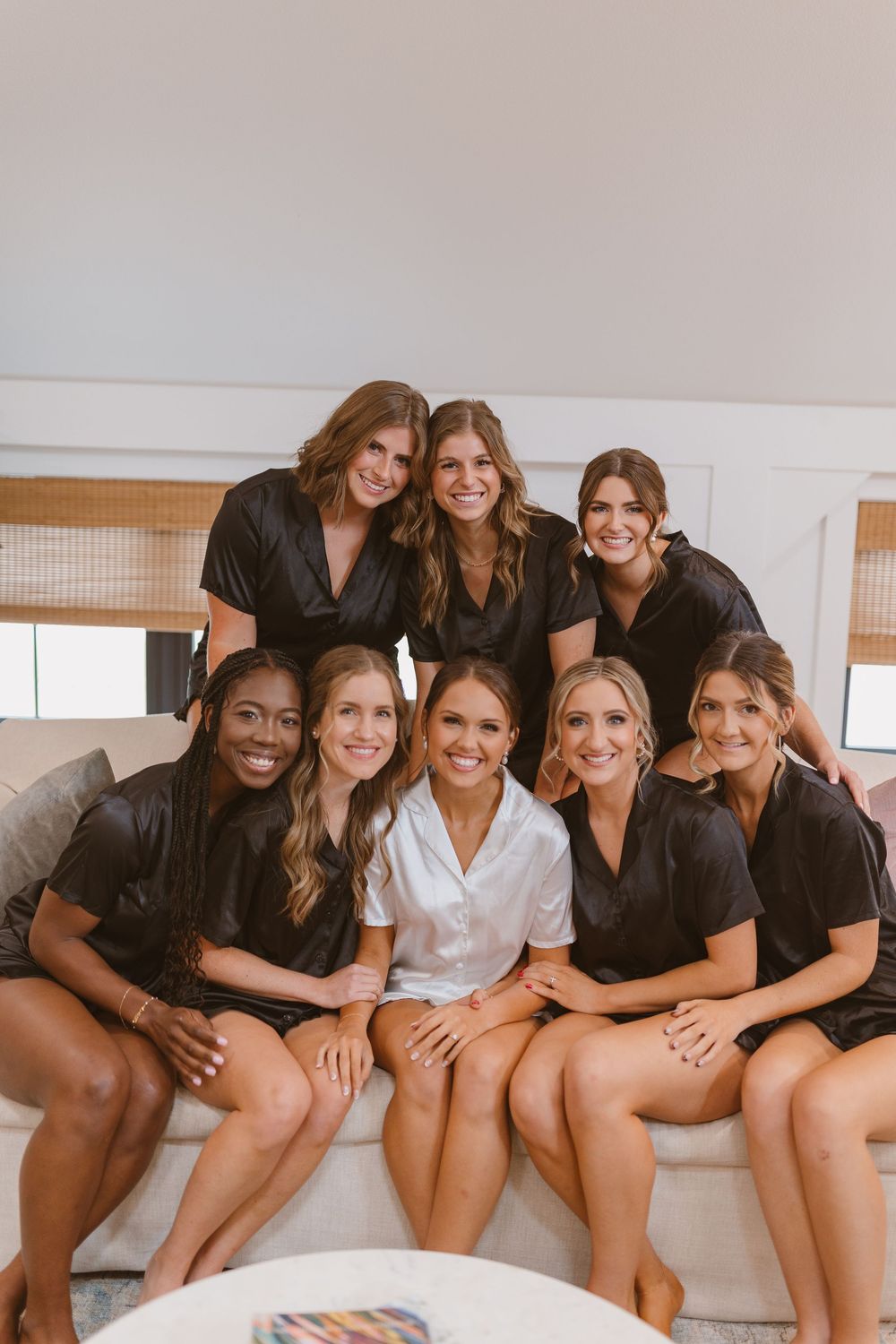Group of friends in matching black robes gather on a couch for pre-wedding photos.