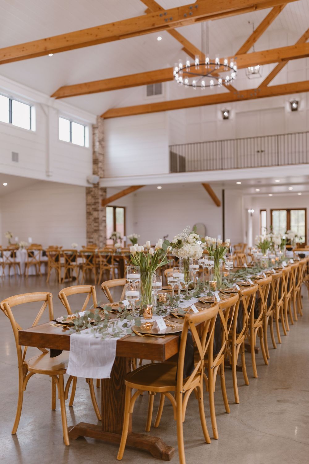 Elegant wedding reception venue with long wooden tables, crossback chairs and rustic ceiling beams.